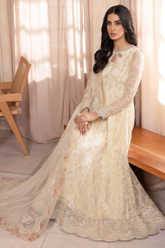 Iqra Aziz sitting in a room wearing a light beige and white embroidered chiffon dress with sleeves and a dupatta. The dress has intricate floral patterns embroidered on it.