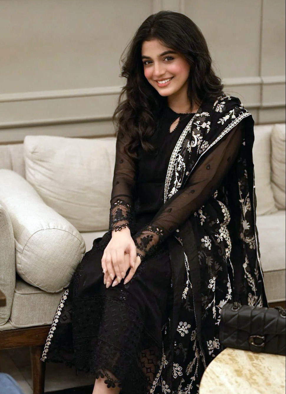 Laiba Khan in black traditional outfit with white patterns sitting on a couch for Eid dresses collection photoshoot
