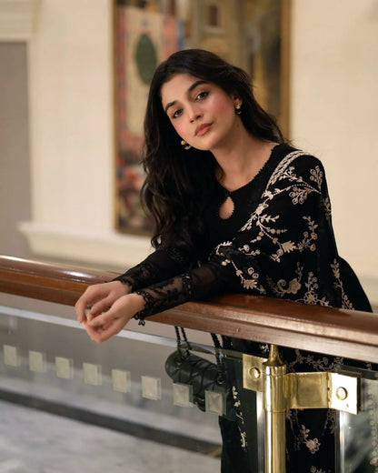 Laiba Khan Pakistani actress in a black and gold embroidered outfit leaning against a railing indoors.